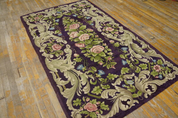 Dark purple rug with sculpted pink rose and sage green scroll patterns on a distressed wood floor.