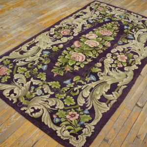Ornate floral rug with a deep purple field and sage green border rests on distressed wooden planks.