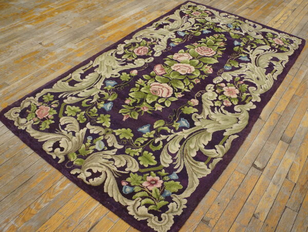 Ornate floral rug with a deep purple field and sage green border rests on distressed wooden planks.