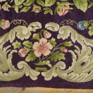 Deep purple rug featuring an ornate border of pale green scrolls and pink floral designs on wood flooring.