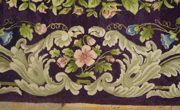 Deep purple rug featuring an ornate border of pale green scrolls and pink floral designs on wood flooring.