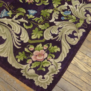 Close-up of a high-pile rug with a purple background, sage green scrolls, and pink and blue flowers, resting on worn wood planks.