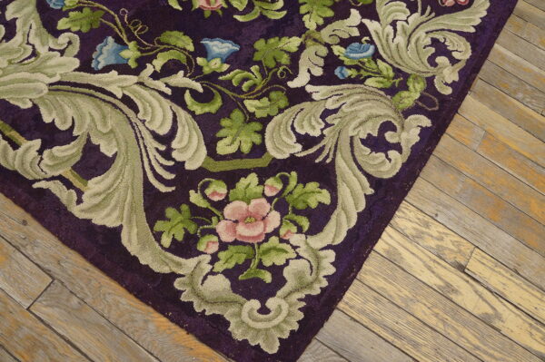 Close-up of a high-pile rug with a purple background, sage green scrolls, and pink and blue flowers, resting on worn wood planks.
