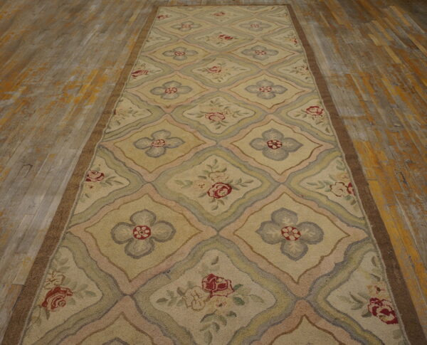 Textured beige runner with a floral diamond pattern in pastel tones rests on distressed hardwood flooring.