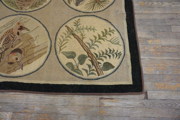 Tan and black border rug featuring circular woodpecker and foliage designs on rustic gray flooring.