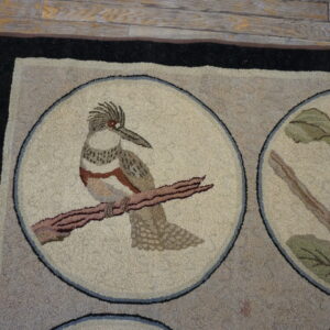 Looped beige and taupe rug featuring bird and nest medallions rests on distressed wood plank flooring.