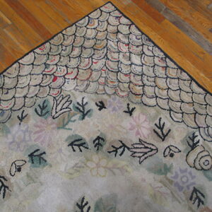 A corner of a textured rug with a light scalloped border and dark botanical shapes on wood flooring.