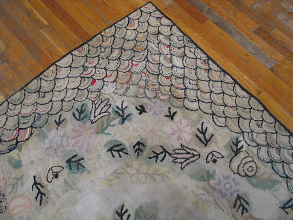 A corner of a textured rug with a light scalloped border and dark botanical shapes on wood flooring.