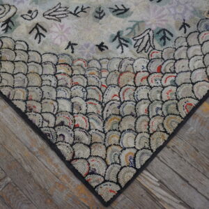 A heavily textured rug featuring a scale border and simple pastel floral motifs rests on rustic gray flooring.