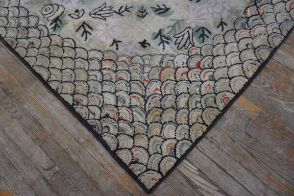 A heavily textured rug featuring a scale border and simple pastel floral motifs rests on rustic gray flooring.