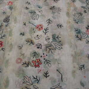 Close-up shows a faded floral pattern on a light rug with a scaled, dark-outlined border.