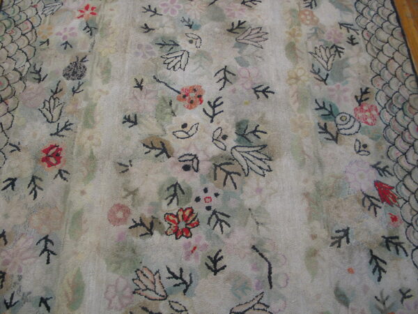Close-up shows a faded floral pattern on a light rug with a scaled, dark-outlined border.