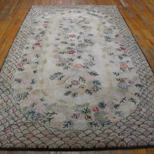 Cream rug with pastel floral motifs and a dark-outlined scalloped border rests on wood flooring.