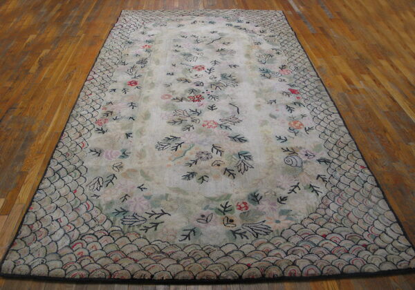 Cream rug with pastel floral motifs and a dark-outlined scalloped border rests on wood flooring.