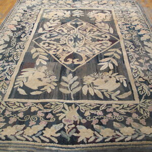 Textured rug in dark blue and beige displays a large medallion and thick floral border on wood flooring.