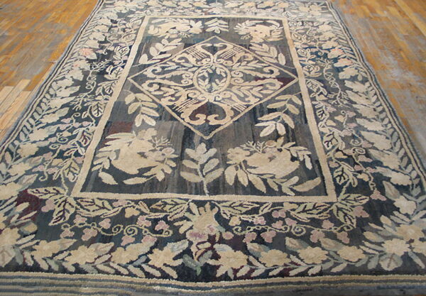 Textured rug in dark blue and beige displays a large medallion and thick floral border on wood flooring.