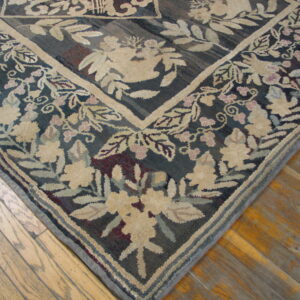 Textured rug corner with beige and pink floral border against a dark background, resting on wood planks.