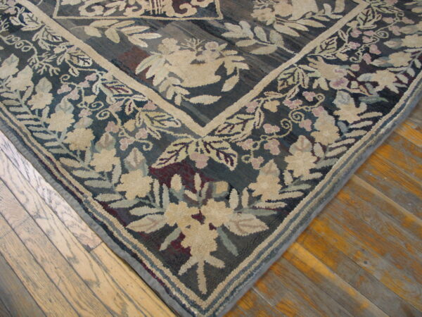 Textured rug corner with beige and pink floral border against a dark background, resting on wood planks.
