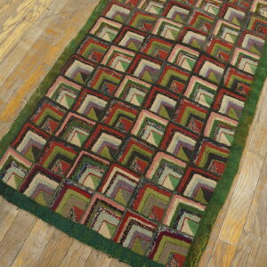 Hooked rug featuring a repeating geometric block pattern in red, green, purple, and cream on a wood floor.