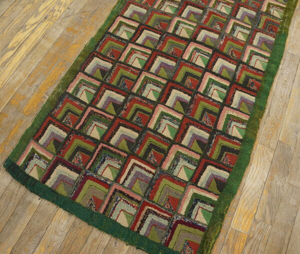 Hooked rug featuring a repeating geometric block pattern in red, green, purple, and cream on a wood floor.