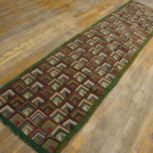 Textured runner with a repeating pattern of multicolored nested L-shapes lies upon distressed light wood plank flooring.
