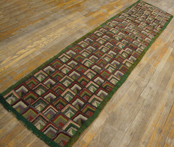 Textured runner with a repeating pattern of multicolored nested l-shapes lies upon distressed light wood plank flooring.