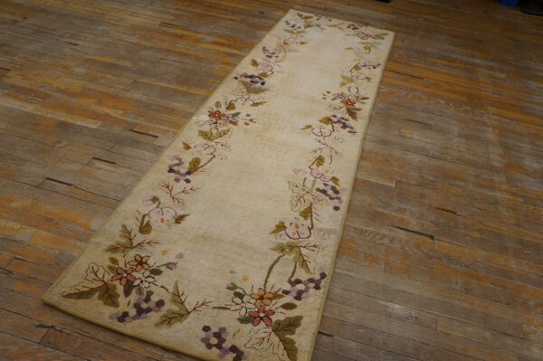 Textured cream runner rug featuring colored floral vine borders on distressed wide plank wood flooring.