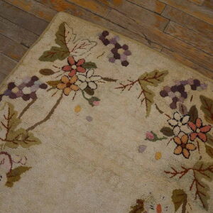 Multicolored floral hooked rug with a cream field rests on distressed, dark wood plank flooring.