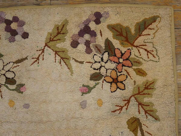 Detail of a textured hooked rug featuring peach, purple, and green floral vine patterns on a cream background near wood.
