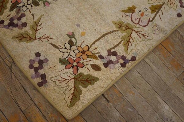 Beige textured rug with pink, purple, and green floral clusters on distressed, wide plank wood flooring.