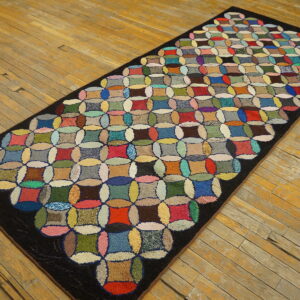 Multicolored hooked runner rug featuring a circular quilt-like pattern on rustic wood floorboards.