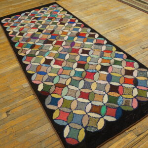 A multicolored, high-pile rug runner with an interlocking geometric pattern rests on distressed yellow-toned wood flooring.