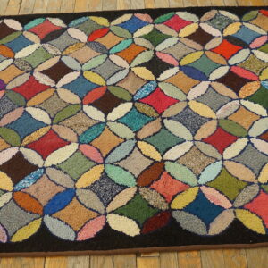 Multicolored hooked rug featuring a highly textured quatrefoil quilt pattern on natural wood flooring.
