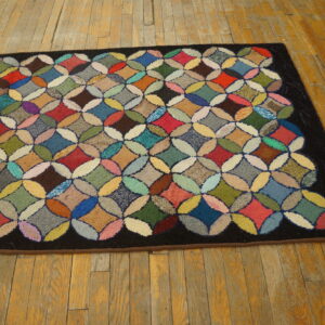 Multicolored hooked rug featuring a geometric circle pattern and a dark border on distressed hardwood floors.