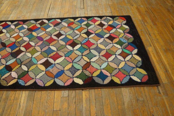 Multicolored hooked rug featuring a geometric circle pattern and a dark border on distressed hardwood floors.