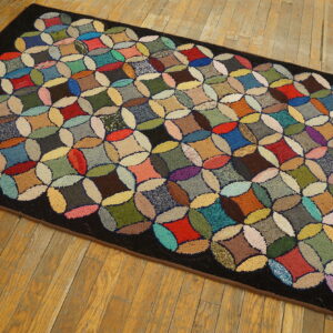 Multicolored runner rug featuring a textured patchwork circle design and a dark border on aged hardwood floors.
