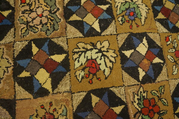 Multicolored looped pile rug featuring a block pattern with tan florals and black geometric starbursts.