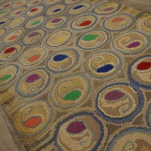Multicolored textured rug with beige and blue concentric rings on distressed light brown wood floors.