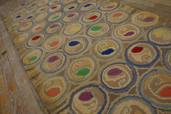 Multicolored textured rug with beige and blue concentric rings on distressed light brown wood floors.