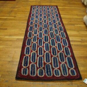 Geometric runner rug with repeating blue and cream ovals on a deep red field, shown on wood planks.