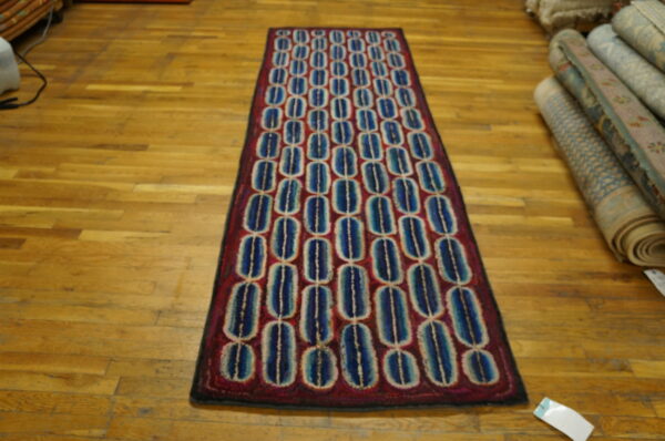 Geometric runner rug with repeating blue and cream ovals on a deep red field, shown on wood planks.