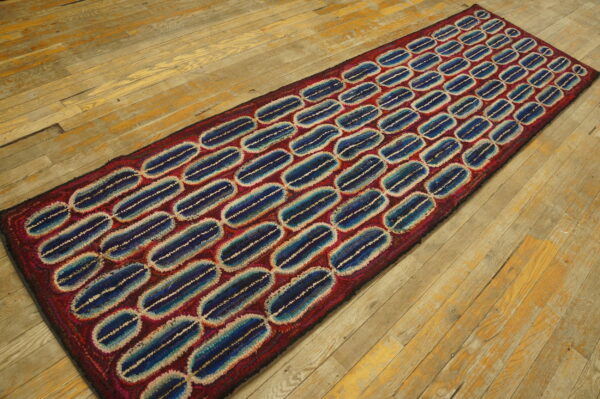 Textured red runner with blue and cream striped oval pattern rests on aged wooden floorboards.