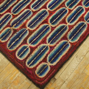 Textured rug with diagonal blue and cream capsule shapes over a red field on light plank wood flooring.
