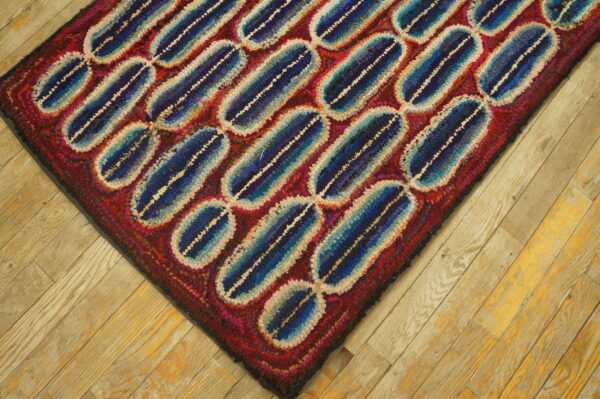 Textured rug with diagonal blue and cream capsule shapes over a red field on light plank wood flooring.