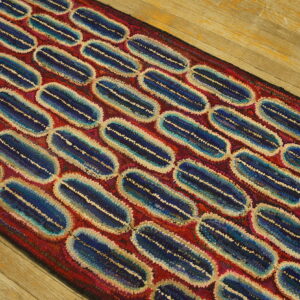 Textured runner rug featuring linked blue and cream oval shapes on a red ground over wood flooring.