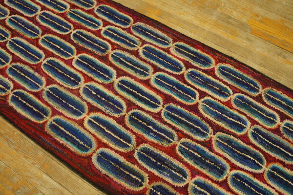 Textured runner rug featuring linked blue and cream oval shapes on a red ground over wood flooring.
