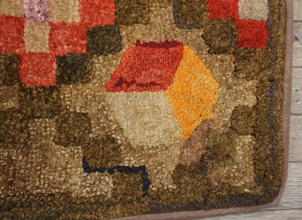 Close-up shows a hooked rug texture with tan, orange, red, and brown geometric patterns on wood flooring.