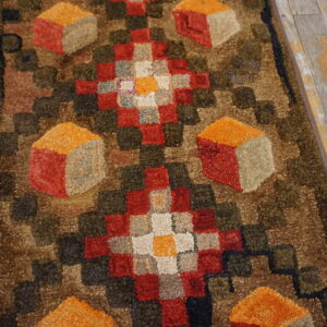Chunky hooked runner featuring geometric diamonds and cube patterns in red, orange, brown, and green on wood flooring.