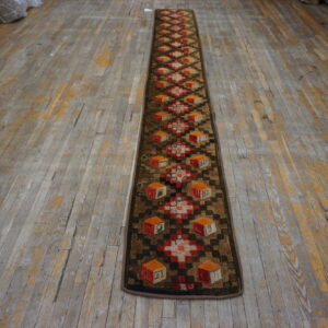 Textured runner with brown, red, and orange geometric cube motifs lies on a distressed wood floor.