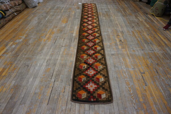 Textured runner with brown, red, and orange geometric cube motifs lies on a distressed wood floor.